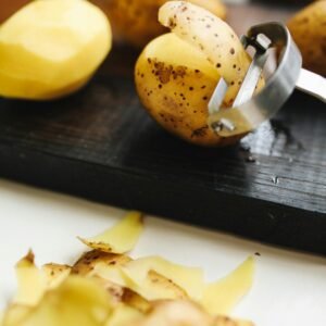 Fresh potatoes being peeled with a peeler on a rustic wooden board.